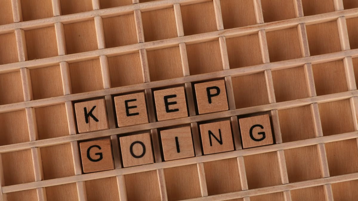 Keep going message spelled with wooden blocks on a wooden grid background.